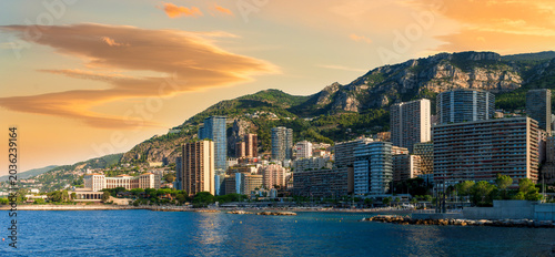 scenic cityscape of embarkment of Monte Carlo city in Monaco with blue sea water bay and amazing tall buildungs and houses along the coast. Urban mideterranean landscape with mountains and cloudy sky.