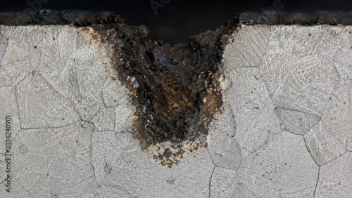 Microscopic examination reveals concerning serious corrosion pitting deeply penetrating an offshore wind turbine metal component showing severe structural degradation and crystalline grain damage