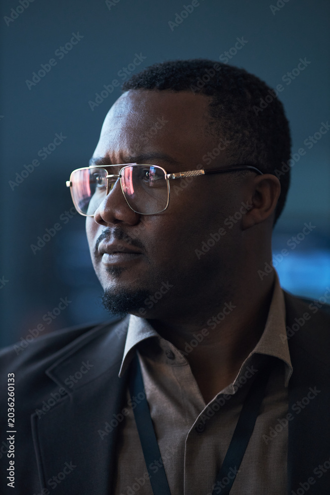 Fototapeta premium Vertical shot of Black middle aged businessman wearing eyeglasses, looking away with focused expression during corporate event. Suitable for leadership, strategy, executive branding