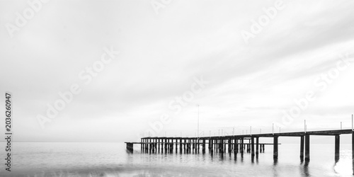 Bild auf Leinwand Minimalist black and white long exposure of a long wooden pier stretching into c