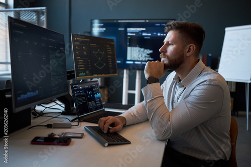 Quadro su tela Caucasian young adult man analyzing cybersecurity data on multiple monitors in office, monitoring code and dashboards