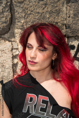 Woman with vibrant red hair relaxing against stone wall