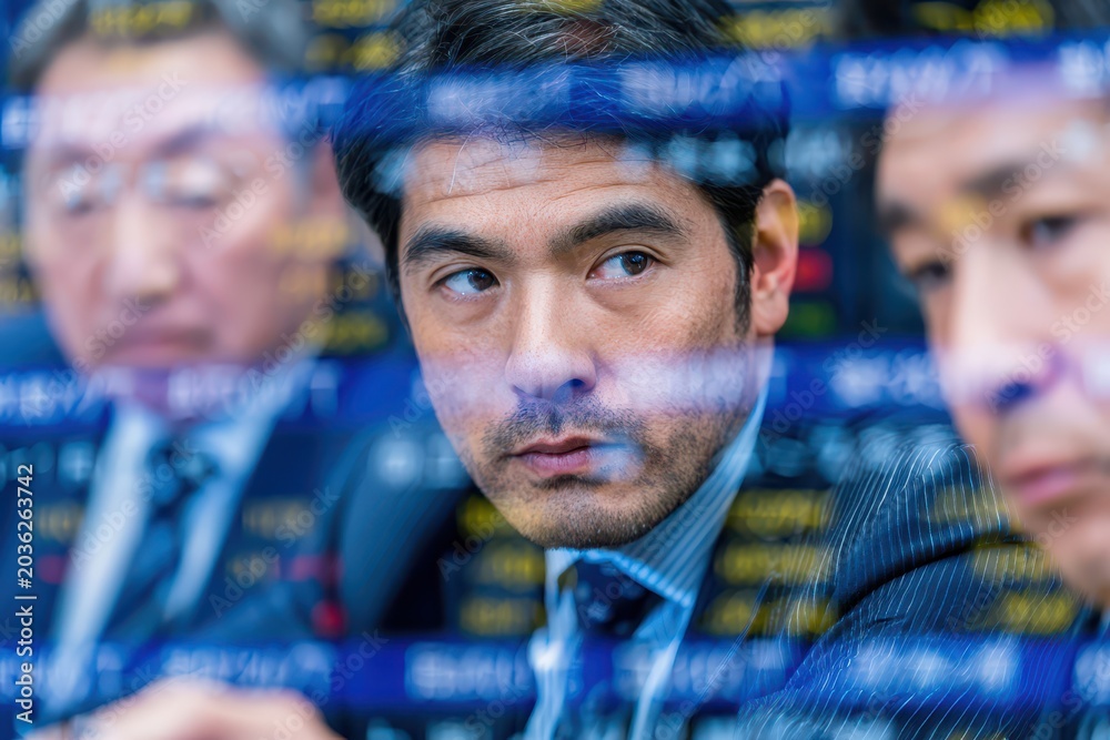 Obraz premium Three businessmen in suits intently watching a stock market data screen with blue digital reflections.