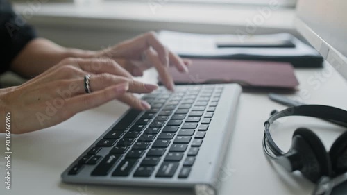 Close up shot of hands of unrecognizable businesswoman typing on keyboard while working at office table with documents and headset