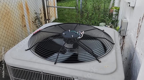 Residential HVAC condenser unit with spinning fan installed outside a building. Climate control equipment providing cooling and air circulation for a home.