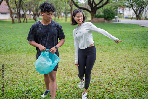 Multicultural Gen Z friends Asian woman and African American mixed race man plogging and collecting trash in green urban park for representing sustainability wellness and positive active lifestyle.