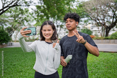 Multicultural Gen Z friends Asian Gen Z woman and African American mixed race man using smartphone taking selfie in green urban park for wellness lifestyle
