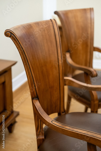 Photos Close up of an elegant classic wooden armchair with a curved backrest, black inlaid details, and a brown leather seat