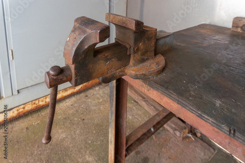 Fotografi Vintage rusty bench vise mounted on a worn metal worktable inside a small workshop, creating an authentic industrial and metalworking scene with carpenter and mechanic tool atmosphere