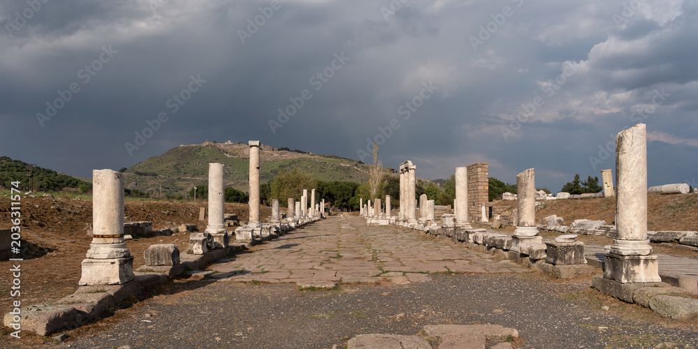Naklejka premium Sacred Way ruins at Asklepion, Pergamon, Bergama, Turkey. Ancient columns line a stone path leading to distant ruins under a blue sky