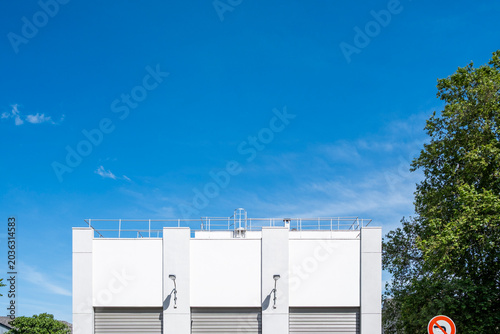 White building rooftop sits against open sky and trees, with industrial equipment marking the urban facade and architecture edge in clear daylight
