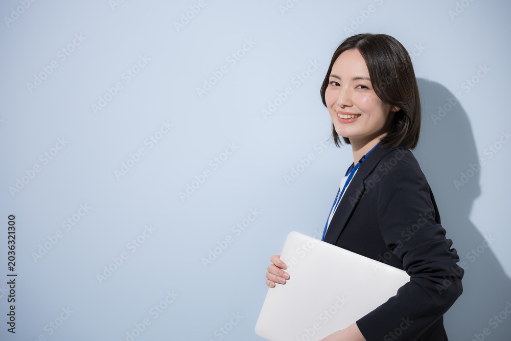 Naklejka premium 水色背景で名札をつけたノートパソコンを持つ働くかわいい女性社員のビジネスとITなどのイメージ カメラ目線笑顔 左にコピースペースあり