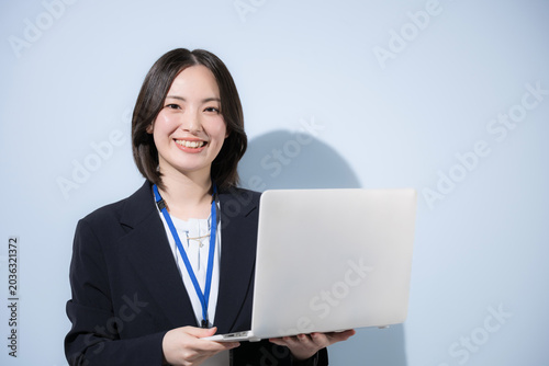 An image of a cute female office worker holding a laptop with a name tag against a light blue background, conveying a business and IT vibe; she is smiling and looking directly at the camera