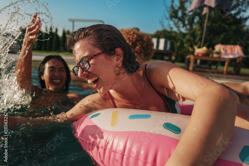 Happy friends splashing water in summer pool