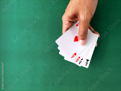 Close-up of a hand holding full set of four aces over a green table.