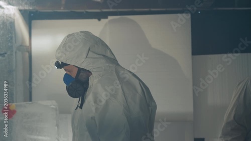 Scientist in hazmat suit inspecting frozen sample inside abandoned house, headlamp beam cutting through frost, gas mask visible, stacked insulated containers, sterile boxes, tense clinical atmosphere