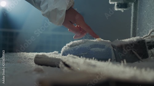 Finger pressing icy button on frozen device, low cold light, sterile sleeve hovering, delicate contact triggers frosty particles, suspenseful lab moment implying critical sample activation
