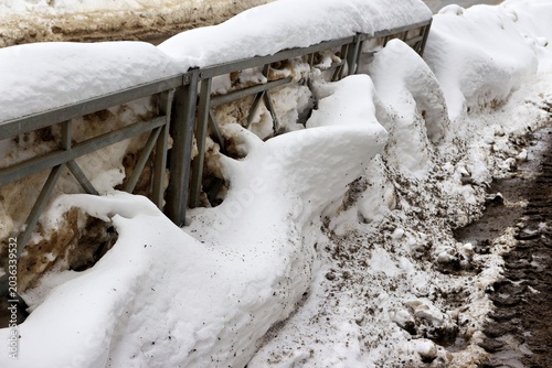 Foto Dirty, melting snow clings to a roadside fence, revealing muddy slush and signs of a late winter thaw