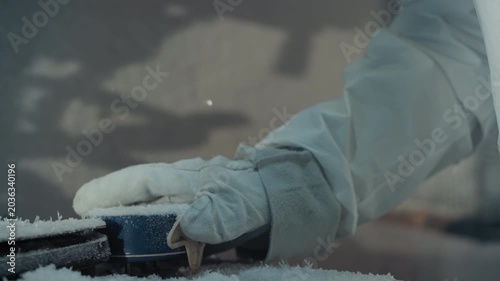 Gloved hand holding sensor device bearded researcher in protective suit examines frostcovered instrument under lamp beam breath visible in cold air methodical inspection by field technician engineer