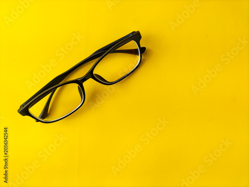Minimalist composition of Black eyeglasses over bright yellow surface.