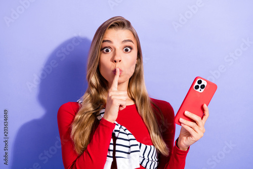Foto Young woman with smartphone making shh gesture and surprised expression holding
