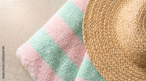Straw hat and striped beach towel on sand under bright sunlight.
