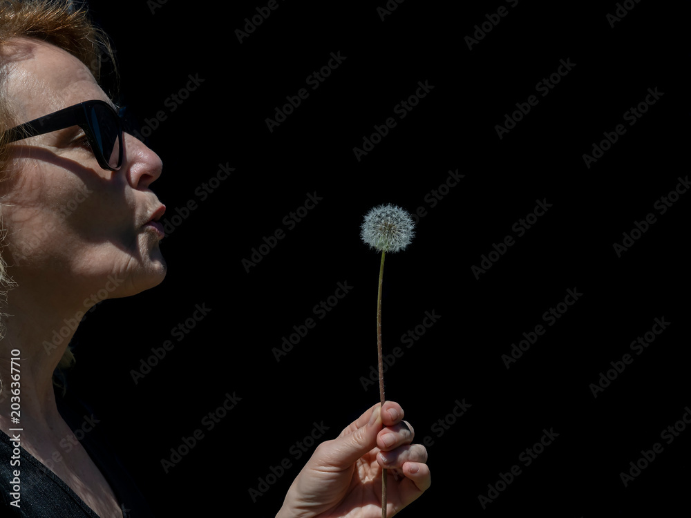 Φωτογραφία A woman wearing sunglasses is about to blow a dandelion on a black background