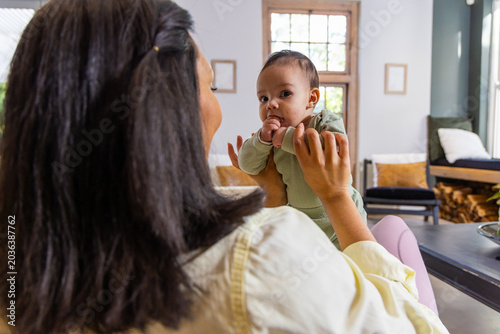 Foto Mother and infant sitting on couch in living room, holding baby wearing green ro