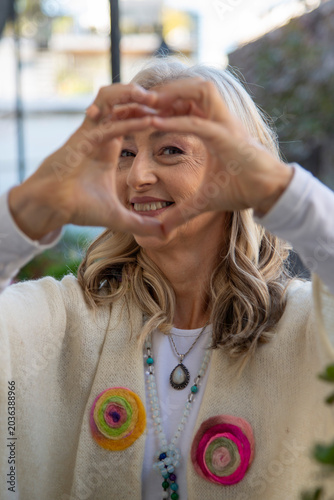 Smiling mature woman looking through heart shaped hands