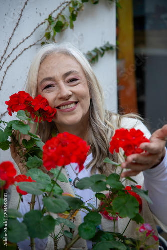 Happy mature woman posing behind red flowers outdoors