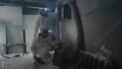 Scientist inspects frozen basement pipe, hazmat operator kneels with flashlight collecting contaminated sample from corroded radiator in derelict house icy debris, frostcovered vent, emergency