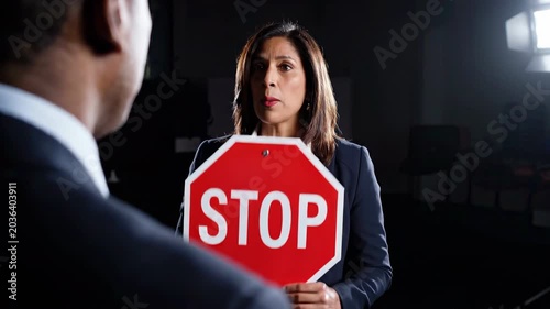 Stop sign businesswoman confrontation harassment workplace boundary warning refusal intimidation conflict, businesswoman holding stop sign facing colleague dark office during tense workplace conflict