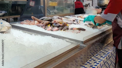 A unrecognisable supermarket employee wearing gloves arranges products on an ice-filled display table, maintaining freshness and an attractive presentation.