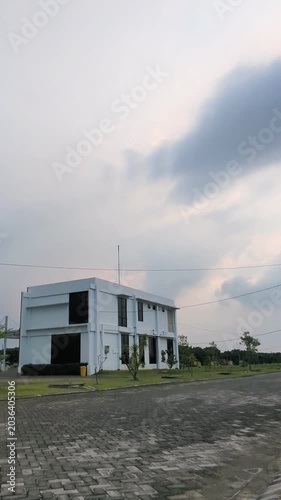 A modern white building stands beside a quiet road under a cloudy sky, creating a calm suburban atmosphere before the rain arrives.
