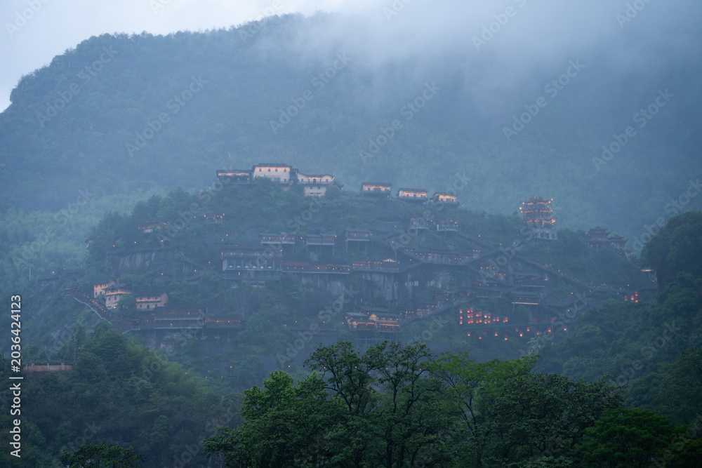 Fototapeta premium Beautiful traditional architecture glowing on the misty mountains of Wangxian Valley Scenic Area in Jiangxi China