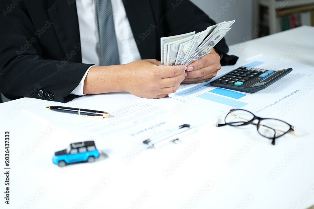 Fototapeta premium A businessman counts money at his desk for car insurance, vehicle maintenance, vehicle purchases, and rentals. Business and transportation concepts