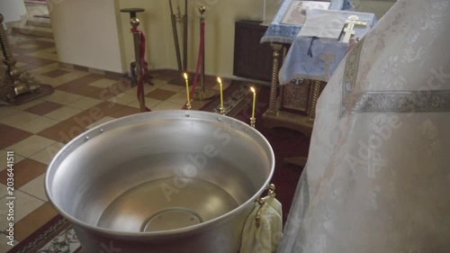Close-up view of a priest hand performing sacrament preparation of water in a baptismal font for holy ritual ceremony in a dimly lit church interior with warm candlelight