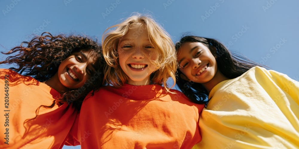 Naklejka premium Smiling trio of children in colorful shirts under blue sky for friendship banner background and youth campaign design
