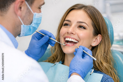 Female patient with open mouth receiving dental care from two professionals in white coats and blue gloves.