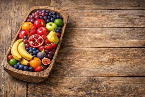 A wooden tray filled with fresh fruits such as bananas, strawberries, and blueberries. The tray is placed on a rustic wooden table.