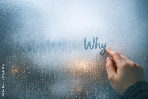 A person writes the word 'why' on a window in bold letters, inspiring curiosity and introspection