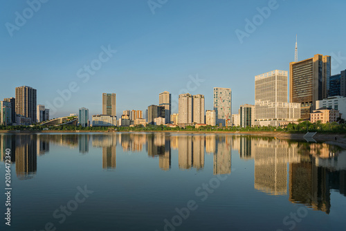 Golden sunlight illuminates modern office towers and residential skyline reflected across Cau Giay Lake in Hanoi, Vietnam.