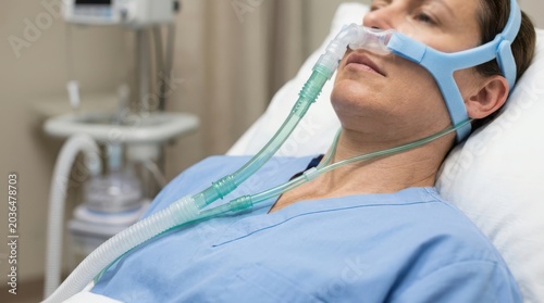 Woman patient wearing CPAP mask in hospital bed, receiving non-invasive ventilation treatment for respiratory support.