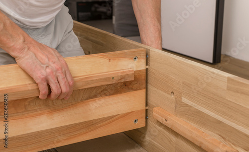Hands assembling a wooden furniture frame. Close up of DIY carpentry with boards, screws, and interior installation work. Home improvement and woodworking project..