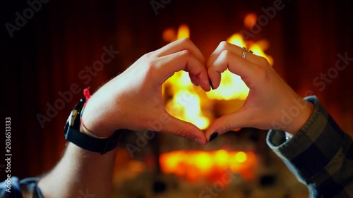 Romantic couple making heart shape with hands. Young happy couple making a heart shape with their hands in front of a cozy fireplace at home