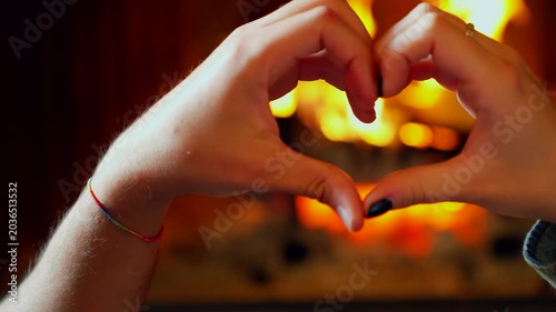 Romantic couple making heart shape with hands. Young happy couple making a heart shape with their hands in front of a cozy fireplace at home