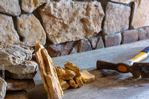 Flagstone for wall cladding and a construction hammer against the background of a fragment of a stone-clad wall