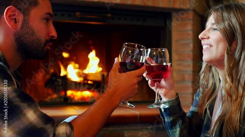 Romantic couple drinking wine by fireplace. Happy young couple toasting with red wine and enjoying a romantic evening by a cozy fireplace