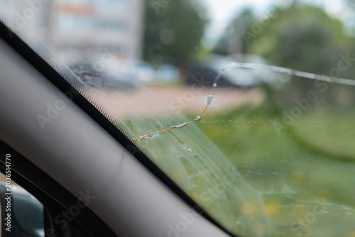 A cracked windshield is seen from inside a vehicle, with a blurred view of a residential area outside