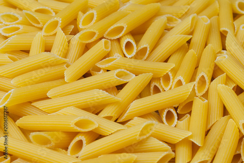 Schilderij op canvas Close-up penne pasta tubes with characteristic ridges and hollow centers scattered together